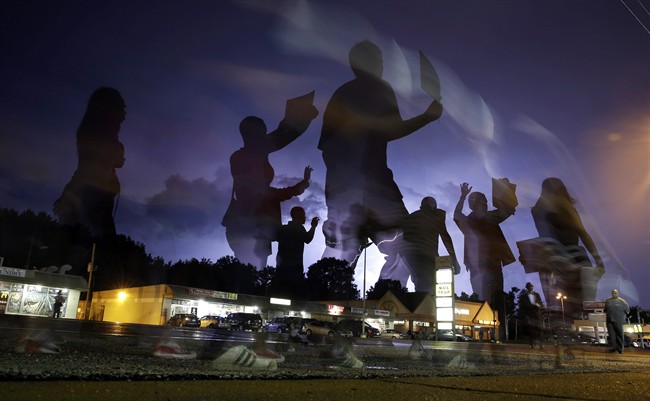 Protesters march in the street as lightning flashes in the distance in Ferguson, Mo. on Wednesday, Aug. 20, 2014. 