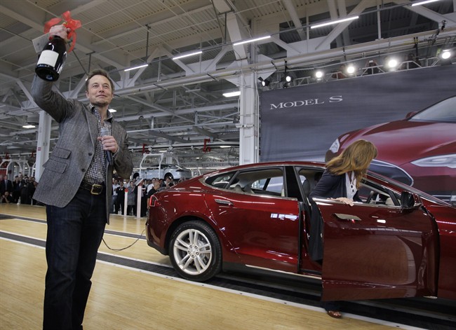 In this June 22, 2012 file photo, Tesla Motors Inc. CEO Elon Musk holds up a bottle of wine given as a gift from one of their first customers, right, during a rally at the Tesla factory in Fremont, Calif.