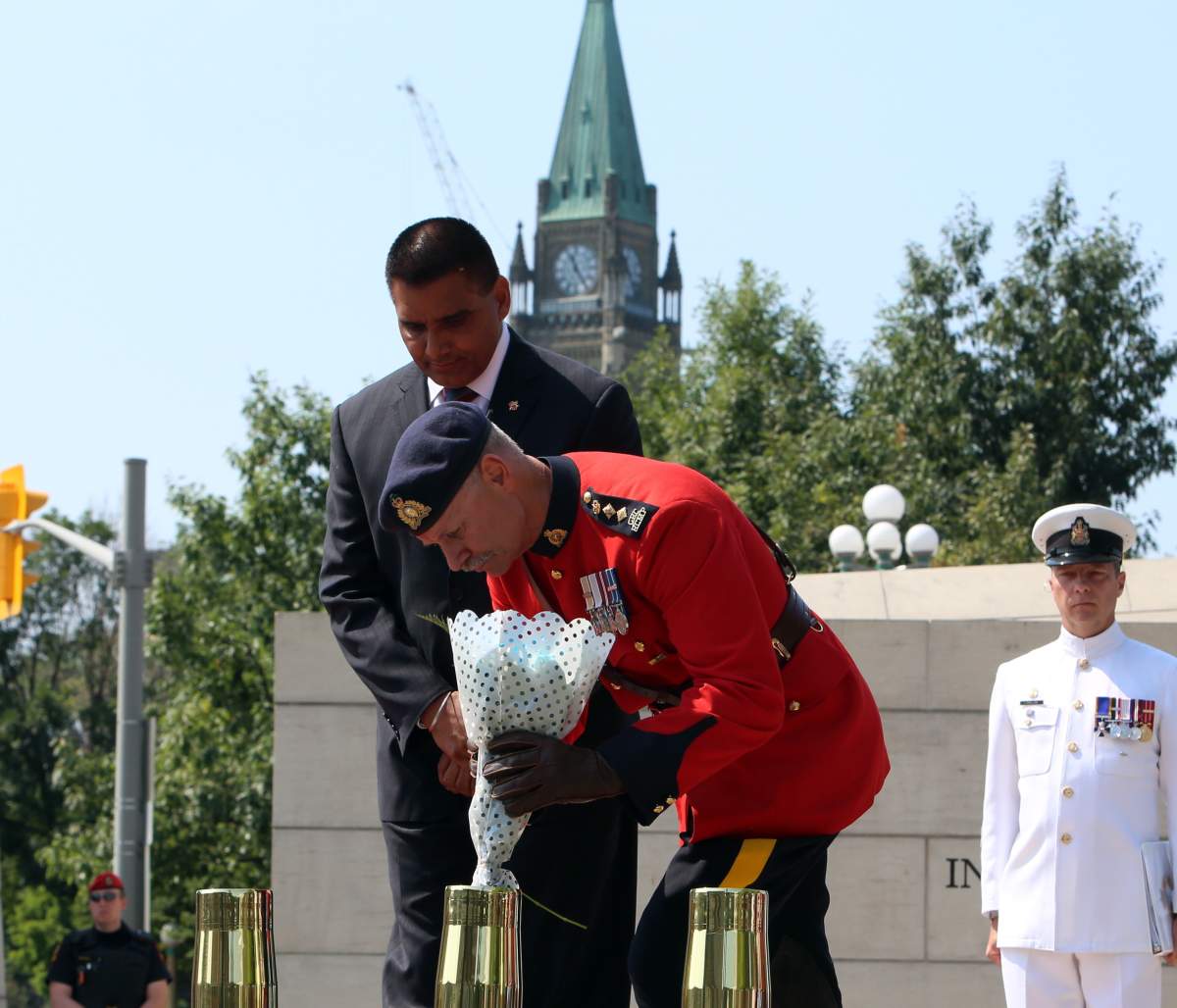 RCMP Chief Superintendent Marion Lamothe, places a bouquet of flowers in a brass shell casing as Parm Gill, parliamentary secretary to minister of veterans affairs (left) looks on onAugust 10,2014.
