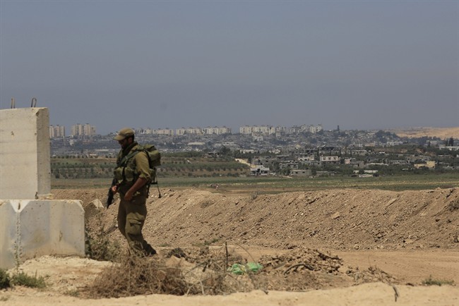 Part of the Gaza Strip looks over an Israeli reserve soldier walking outside a military post near the Israel Gaza border on Thursday, Aug. 7, 2014.