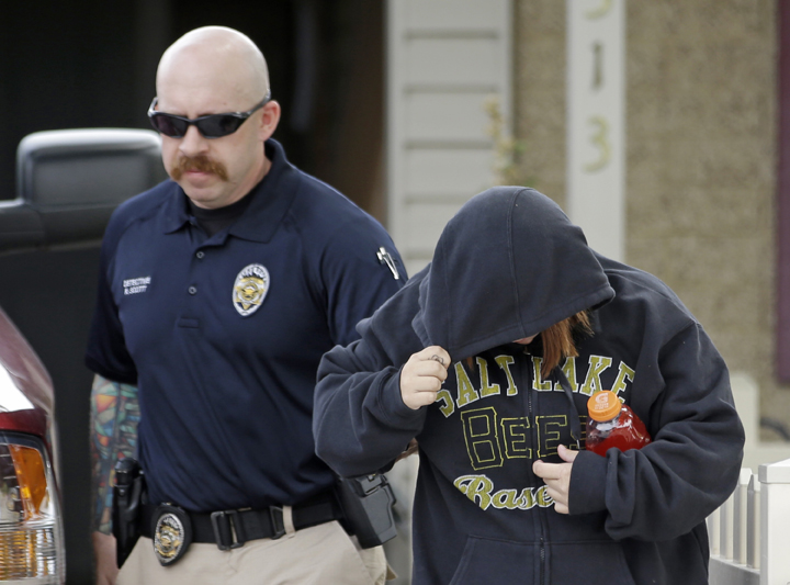 A unidentified woman is escorted from a home by a police officer after a baby was found in a garbage can in Kearns, Utah on Tuesday, Aug. 26, 2014. 