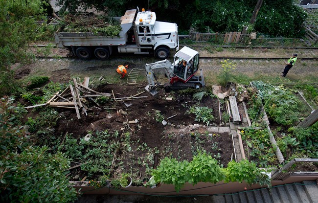 A Canadian Pacific Rail police officer, right, stands by as workers remove community gardens from a stretch of abandoned CP Rail line in Vancouver, B.C., on Thursday August 14, 2014.