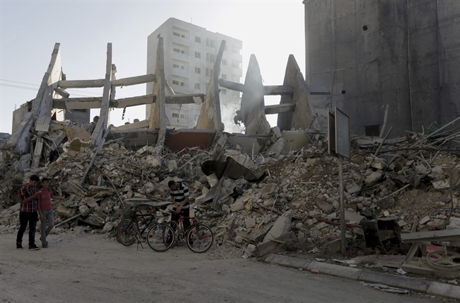Palestinians walk next to the rubble of the 15-storey Basha Tower that collapsed from early morning Israeli airstrikes in Gaza City, in the northern Gaza Strip, Tuesday, Aug. 26, 2014. 