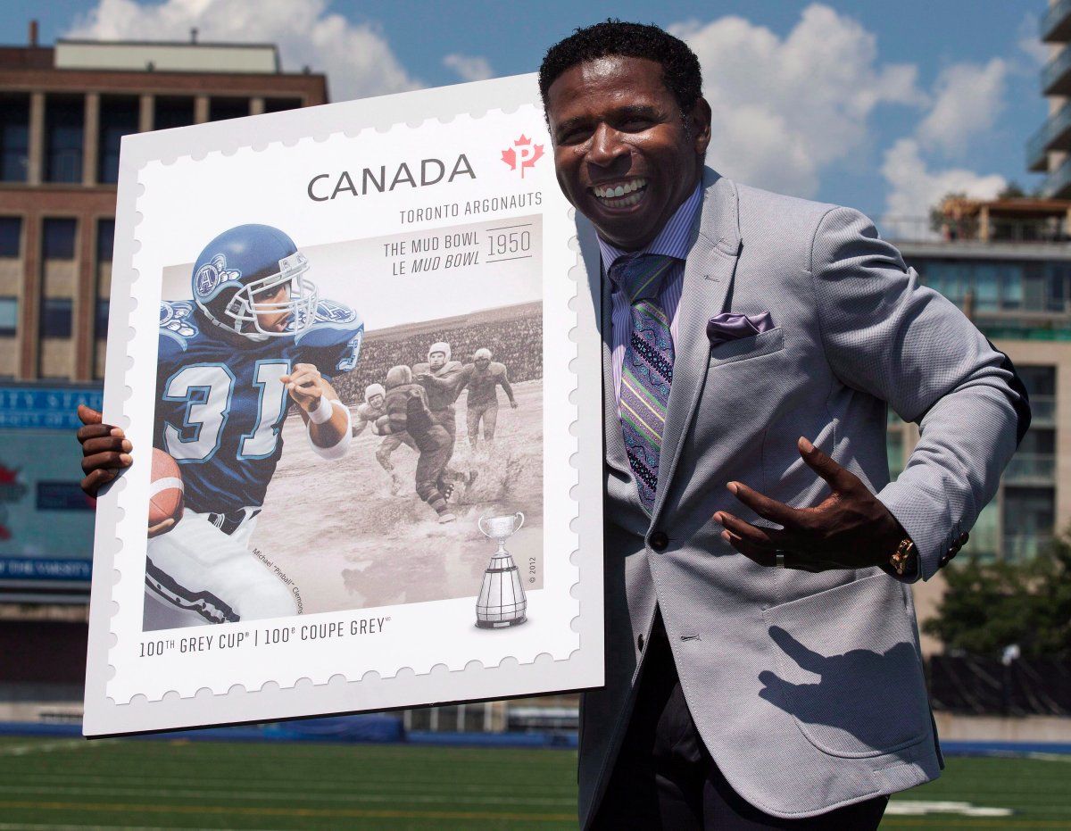 Toronto Argonauts Vice-Chair and former Argos player and head coach Michael "Pinball" Clemons poses for a photo while holding a stamp featuring him as part of a commemorative collection celebrating the CFL's upcoming 100th Grey Cup Game at a news conference in Toronto on Monday, August 13, 2012.