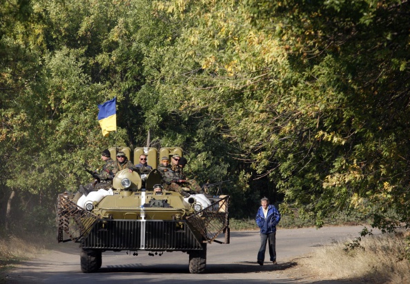 A man looks on as Ukrainian servicemen sitting atop of an Armoured Personnel Carrier drive past during a patrol in Donetsk region on September  15, 2014. 