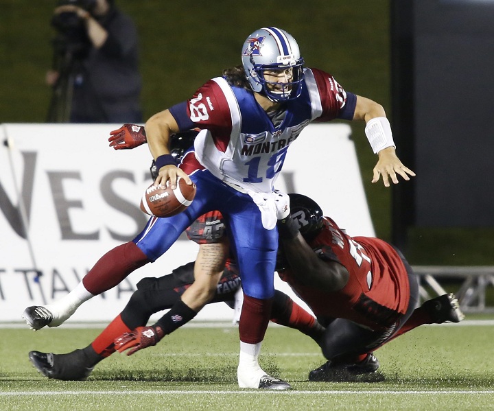 The Montreal Alouettes quarteback Jonathan Crompton fends off a tackle by the Ottawa Redblacks Jonathan Williams, right, and Travis Brown, back, during second quarter CFL action in Ottawa on Friday, September 26, 2014.