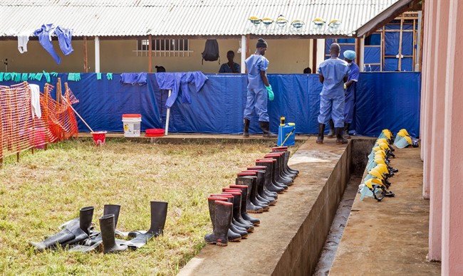 Healthcare workers, rear, clean Ebola virus prevention gear at the Hastings Police training school, used as a Ebola virus treatment center with over a hundreds beds in the village of Hastings, Sierra Leone, Saturday, Sept. 20, 2014. (AP Photo/ Michael Duff).