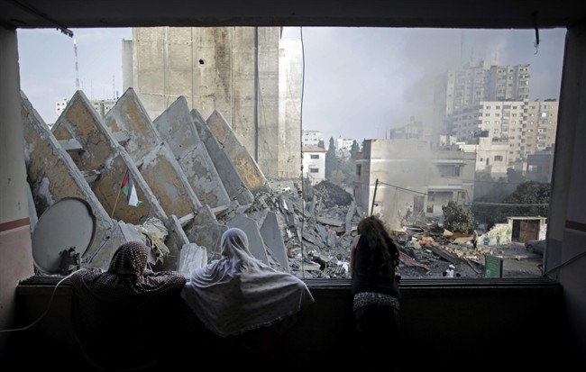 In this Tuesday, Aug. 26, 2014 file photo, a Palestinian family looks from a window at the rubble of the collapsed 15-story Basha Tower following early morning Israeli airstrikes in Gaza City. 