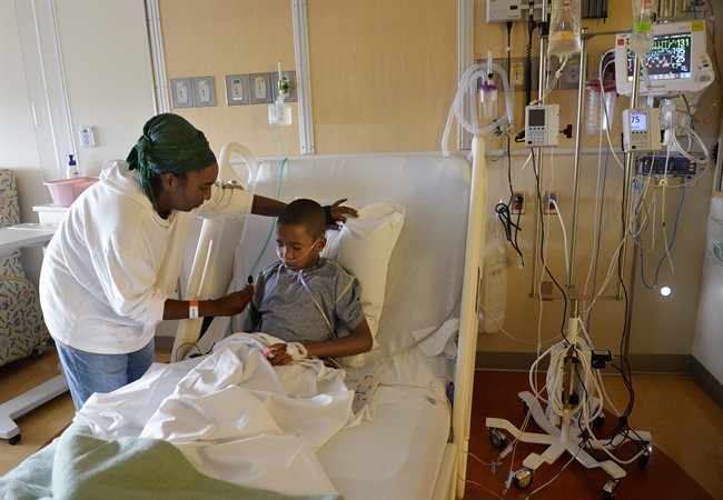 In this Monday, Sept. 8, 2014 photo, Melissa Lewis, of Denver, helps her son, Jayden Broadway, 9, as he coughs in his bed at the Children's Hospital Colorado in Aurora, Colo.