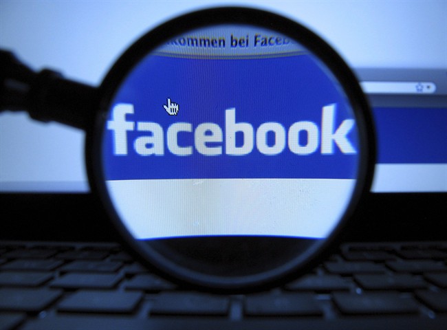 A magnifying glass is posed over a monitor displaying a Facebook page.