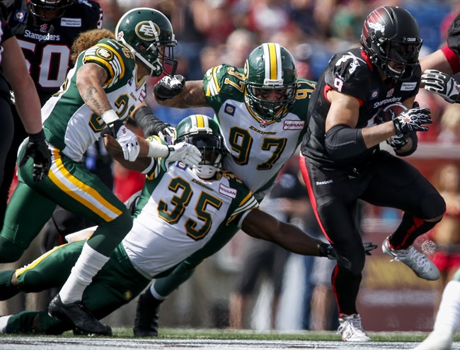 Edmonton Eskimos' Aaron Grymes, left, and Rennie Curran, second form left, and Eddie Steele, centre, bring down Calgary Stampeders' Jon Cornish, during first half CFL football action in Calgary, Alta., Monday, Sept. 1, 2014.