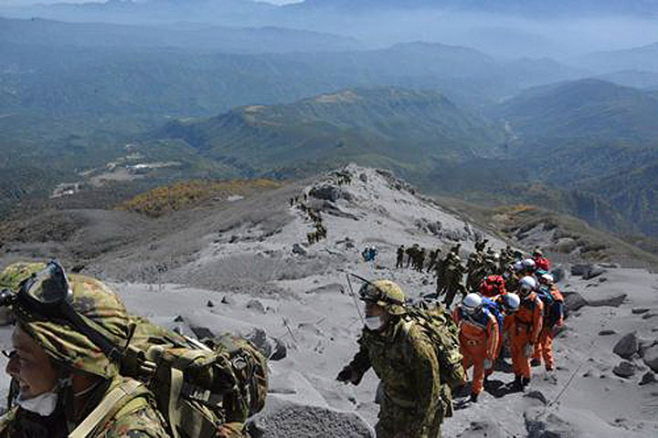 In this photo taken Sunday, Sept. 28, 2014 and released by the Japan Ground Self-Defense Force (JGSDF), JGSDF personnel and fire fighters climb the ash-covered slope, heading for the summit of Mount Ontake to rescue people who have been trapped in the mountaintop lodge during the eruption, one day after the volcano became active in central Japan.