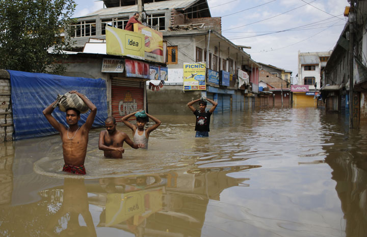 Indian migrant workers wade through receding flood waters with their belongings on their heads in Srinagar, Indian controlled Kashmir, Sunday, Sept. 14, 2014. 