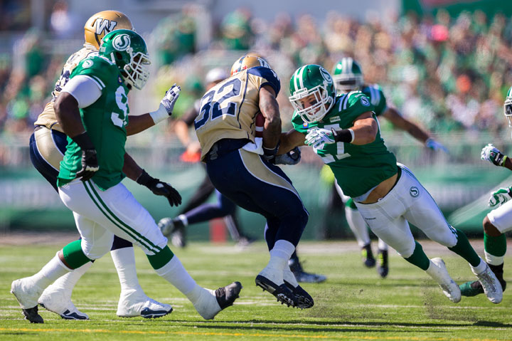 Brian Peters #27 of the Saskatchewan Roughriders dives to make a tackle on Nic Grigsby #32 of the Winnipeg Blue Bombers in a game between the Winnipeg Blue Bombers and Saskatchewan Roughriders in week 10 of the 2014 CFL season at Mosaic Stadium on August 31, 2014.