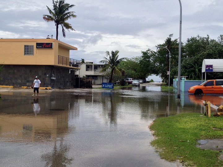 A person walks through a flooded area near the beach in Tumon Guam, Monday, Oct. 6, 2014. A typhoon whipped the Mariana Islands, including Guam, with high winds and heavy rain. As conditions improved, Guam officials shut down the island's storm center, the airport resumed full operations, and government agencies and many businesses began reopening. 