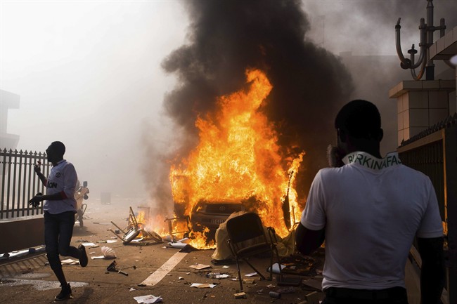 In this photo taken Thursday, Oct. 30, 2014, a car burns after being set alight by protesters outside the parliament building in Burkina Faso as people protest against their longtime President Blaise Compaore who seeks another term, in Ouagadougou, Burkina Faso. 