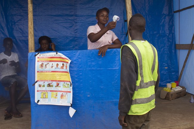 In this photo taken on Tuesday, Oct. 21, 2014, a health worker takes the temperature of a man, right, as part of the countries fight against the spread of the Ebola virus, on the Masiaka Highway, forming part of a trans-West African highway, which links all West African States, on the outskirts of the capital city of Conakry, Guinea.