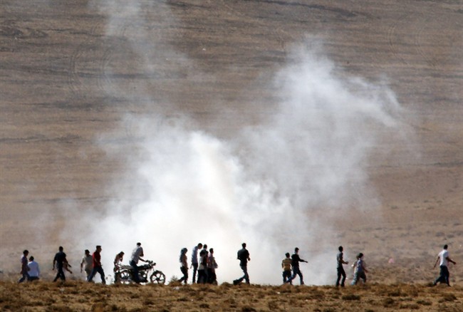 Turkish Kurds run in the outskirts of Suruc, at the Turkey-Syria border, to avoid the effect of tear gas fired by Turkish forces to disperse them after they gathered as fighting intensified between Syrian Kurds and the militants of Islamic State group, in nearby Kobani, Syria, Tuesday, Oct. 7, 2014. Kobani.