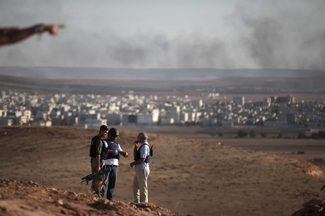 Members of the media talk with a Turkish soldier, left, on a hilltop on the outskirts of Suaruc, at the Turkey-Syria border, overlooking Kobani, Syria, background, during fighting between Syrian Kurds and the militants of Islamic State group, Wedesday, Oct. 15, 2014. 