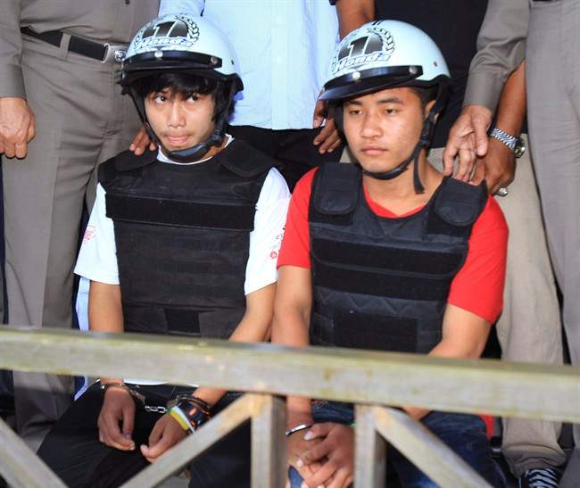 Workers from Myanmar, Saw, left, and Win, sit together, escorted by a Thai police officer, during a press conference in Koh Tao island, Surat Thani province. Thailand, Friday, Oct. 3, 2014. Thai police have arrested the two Myanmar workers they say confessed to killing a pair of British tourists on a beach in the southern Thailand last month.