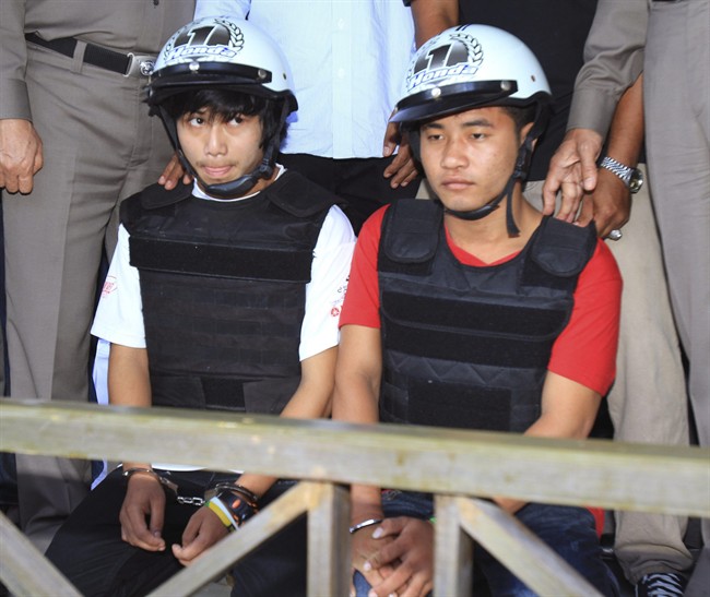 Workers from Myanmar, Saw, left, and Win, sit together, escorted by a Thai police officer, during a press conference in Koh Tao island, Surat Thani province. Thailand, Friday, Oct. 3, 2014. Thai police have arrested the two Myanmar workers they say confessed to killing a pair of British tourists on a beach in the southern Thailand last month.