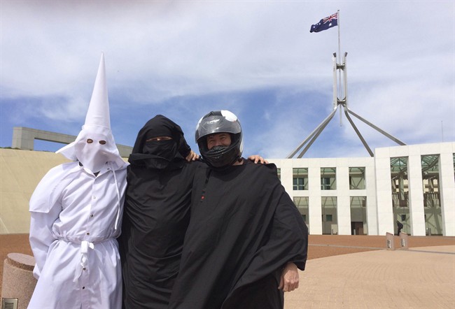 Three men wearing a Ku Klux Klan hood, a niqab and a motorcycle helmet pose for a photo outside Australia's Parliament House in Canberra, Monday, Oct. 27, 2014.
