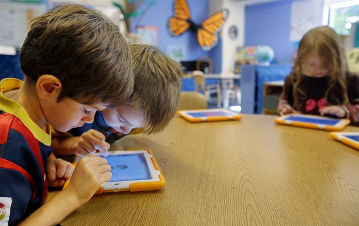 In this Thursday, Sept. 18, 2014 photo, Aiden Crott, 7, center, helps Daniel Hernadez, 5, with his ScratchJr iPad program while Talia Levitt, 7, right, works with hers at the Eliot-Pearson Children's School in Medford, Mass. (AP Photo/Stephan Savoia).