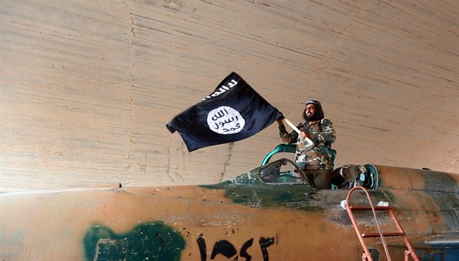 This undated image posted on Aug. 27, 2014 by the Raqqa Media Center of the Islamic State group, a Syrian opposition group, shows a fighter of the Islamic State group waving their flag from inside a captured government fighter jet following the battle for the Tabqa air base, in Raqqa, Syria.