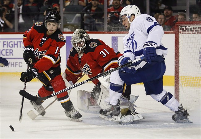 Tampa Bay Lightning Tyler Johnson, right, fights for the puck as Calgary Flames Johnny Gaudreau, left, swats it away while goalie Karri Ramo, from Finland, looks on during second period NHL hockey action in Calgary, Tuesday, Oct. 21, 2014.