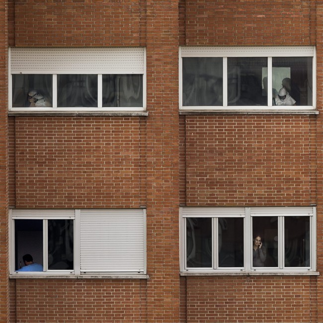 Medical practitioners wearing protective clothing work while Javier Limon, the husband of the nursing assistant infected with Ebola, is seen through a window, lower left, while another isolated girl talks on her phone inside an isolated ward on the sixth floor of the the Carlos III hospital in Madrid, Spain, Friday, Oct. 10, 2014.