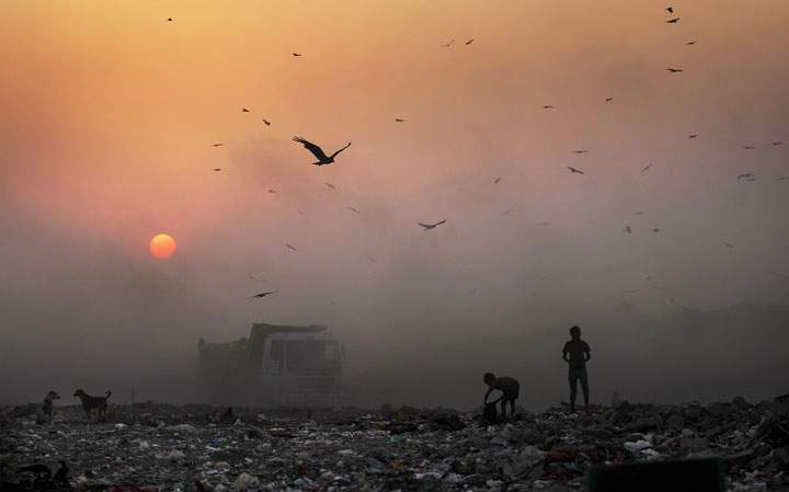 A thick blanket of smoke is seen against the setting sun as young ragpickers search for reusable material at a garbage dump in New Delhi, India, Friday, Oct. 17, 2014.