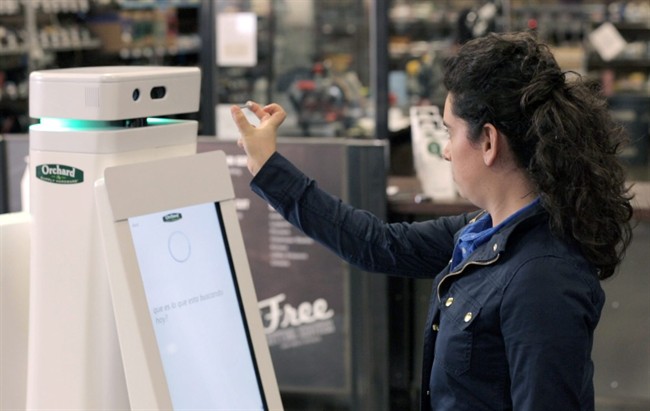 In this undated image provided by Lowe\'s, a woman holds a nail up to be scanned by an OSHbot robot. The robots are equipped with 3D cameras so they can scan and identify items.
