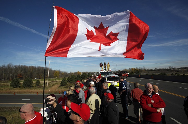 Crowds wave Canadian flags on an overpass at the Veterans Memorial Highway waiting for a procession transporting the body of Cpl. Nathan Cirillo to pass by in Ottawa on Friday, October 24, 2014.