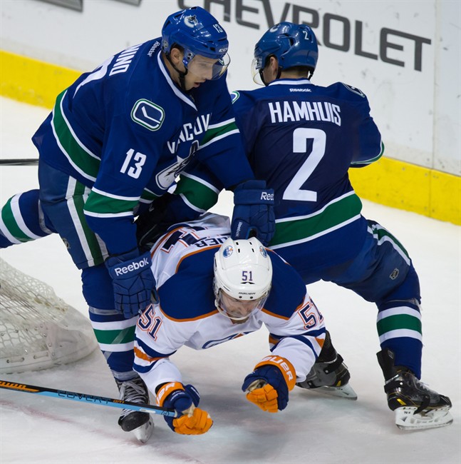Vancouver Canucks' Nick Bonino, left, and Dan Hamhuis, right, check Edmonton Oilers' Anton Lander, of Sweden, during the third period of a pre-season NHL hockey game in Vancouver, B.C., on Saturday October 4, 2014.