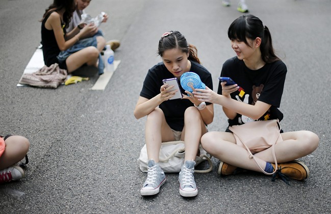 Student pro-democracy activists use their smartphones while sitting on the streets near the government headquarters, Thursday, Oct. 2, 2014 in Hong Kong. The Chinese government might be using smartphone apps to spy on pro-democracy protesters in Hong Kong, a U.S. security firm says. The applications are disguised as tools created by activists to protests, said the firm, Lacoon Mobile Security. The firm said that once downloaded, they give an outsider access to the phone's address book, call logs and other information.