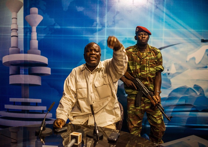 Burkina Faso army Gen. Kwame Lougue, center, with a armed guard at the state television studios, after he entered without speaking to journalists who were waiting  for a announcement by opposition politician Saran Sereme, shorty after gun shots were heard outside the building in Ouagadougou, Burkina Faso, Sunday, Nov. 2, 2014.