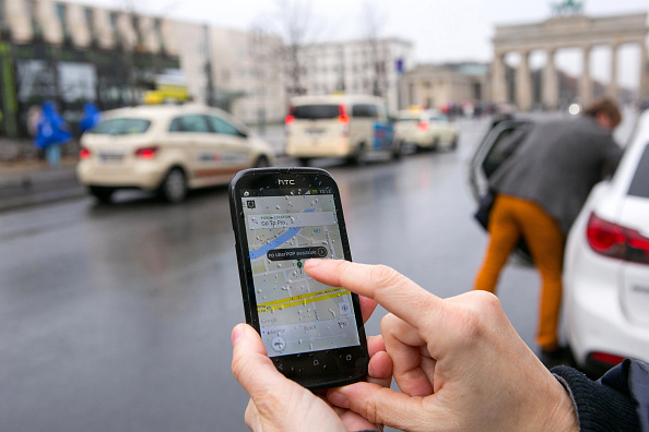 A smartphone displays the Uber Technologies Inc. UberPop car service application (app) in this arranged photograph as taxis and the Brandenburg Gate stand beyond in Berlin, Germany, on Monday, Nov. 24, 2014. 