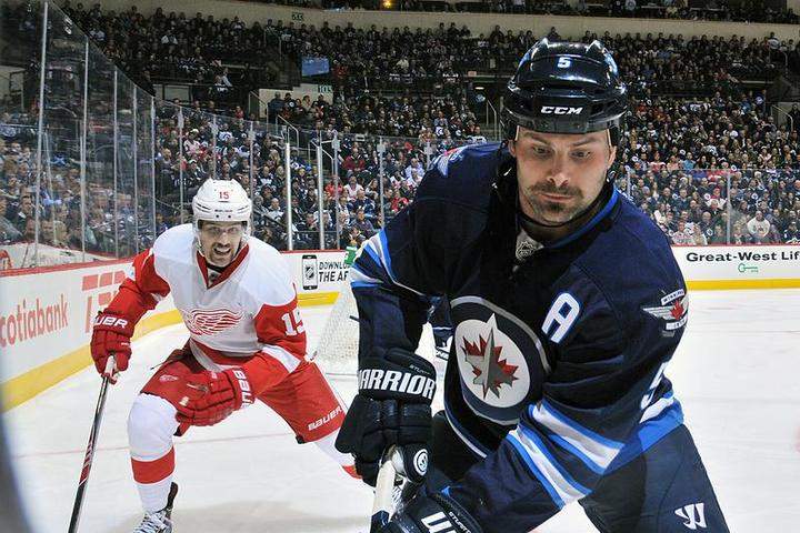 Winnipeg Jet Mark Stuart plays the puck along the boards as Detroit Red Wing Riley Sheahan is in hot pursuit.