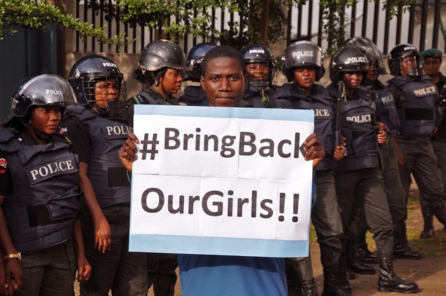 FILE-In this file photo taken on Tuesday, Oct. 14, 2014, a man poses with a sign in front of police officers in riot gear during a demonstration calling on the government to rescue the kidnapped girls of the government secondary school in Chibok, in Abuja, Nigeria.