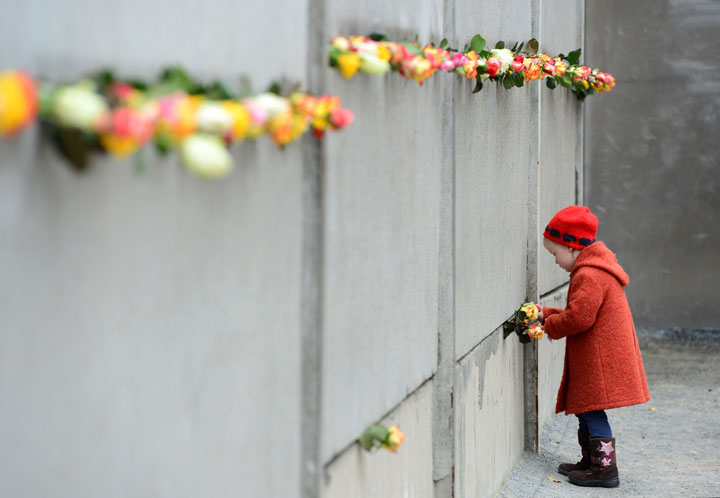 A young girl slips a rose in a preserved segment of the Berlin Wall during the commemorations to mark the 25th anniversary of the fall of the Berlin Wall at the Berlin Wall Memorial in the Bernauer Strasse in Berlin, on November 9, 2014.