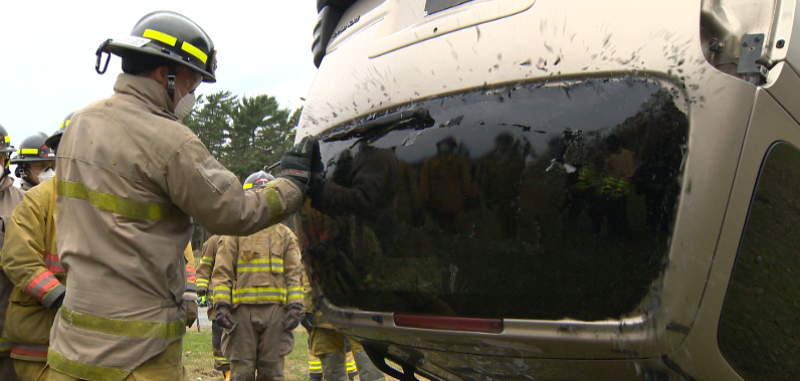 A student practices breaching a car window that has flipped upside down.