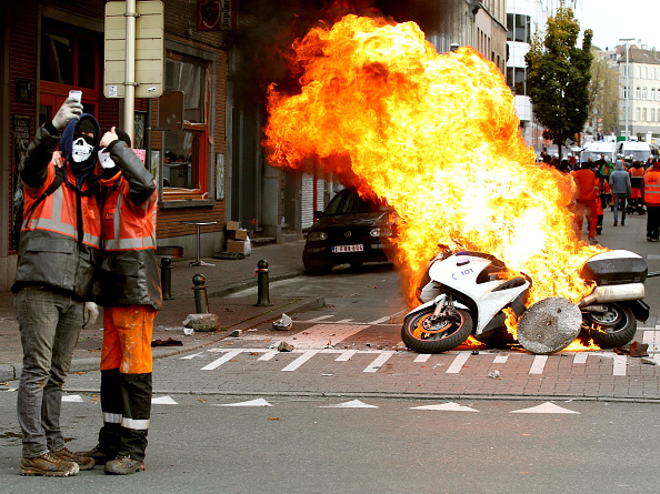 Two people take a selfie in front of a burning police motorbike in Brussels, on November 6, 2014. Belgians are protesting government policies that will extend the pension age, contain wages and cut into public services.