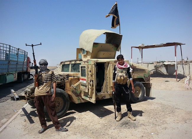 In this file photo taken Thursday, June 19, 2014, Islamic State group militants stand by a captured Iraqi army Humvee at a checkpoint outside Beiji refinery, some 250 kilometers north of Baghdad, Iraq. 