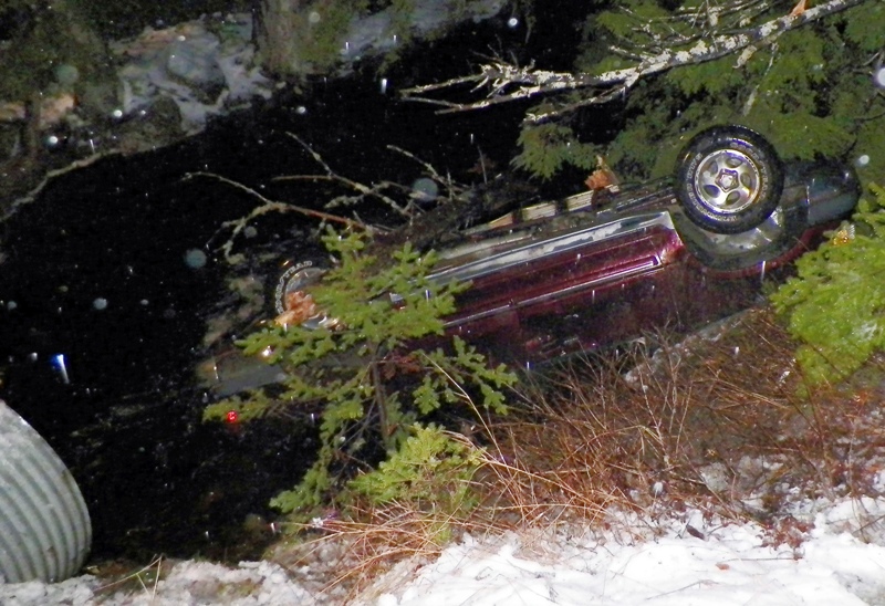 In this Nov. 17, 2014 photo provided by Maine State Police, an SUV rests upside down in water alongside Route 6 in Kossuth Township, Maine, after Stephen McGouldrick lost control of it on the icy road. Police said Leo Moody, of Kingman, Maine, crawled into the SUV and used a knife to cut the straps off a submerged car seat to pull an infant to safety. 