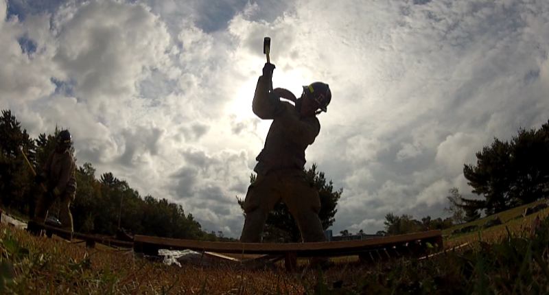 A student uses a sledgehammer to breakthrough a wooden crate.