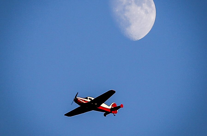 A small vintage airplane from the late 1940's flies past the moon near Cremona, Alta., Monday, July 7, 2014.