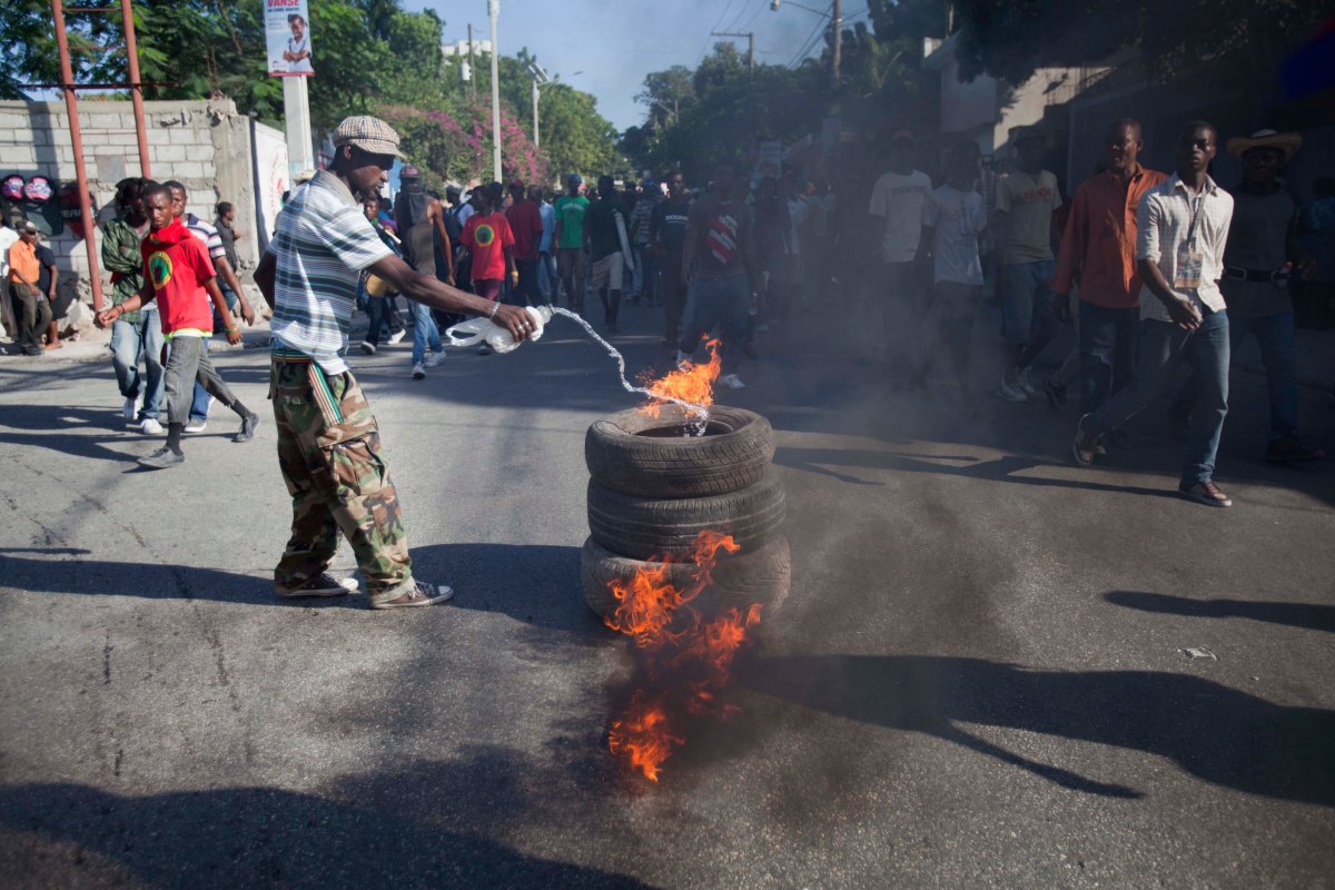 An anti-government protester pours gas on burning tires as demonstrators block a road and call for the resignation of Haitian President Michel Martelly in Port-au-Prince, Saturday, Dec. 6, 2014.