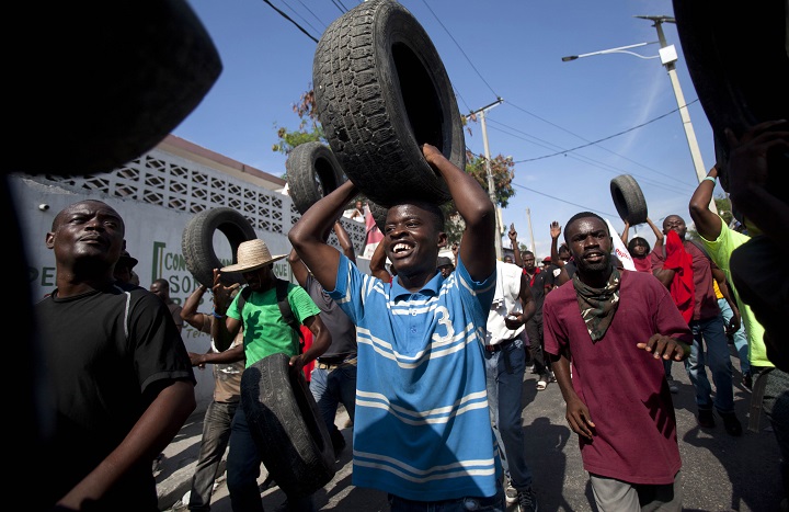 Anti-government protesters carry tires to use for burning road blocks in Port-au-Prince, Haiti, Saturday, Dec. 13, 2014. 