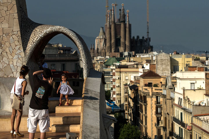 A couple take pictures of their daughter at the roof of the building 'La Pedrera' or 'Casa Mila' of Antoni Gaudi with La Sagrada Familia on the background on July 24, 2013 in Barcelona, Spain.
