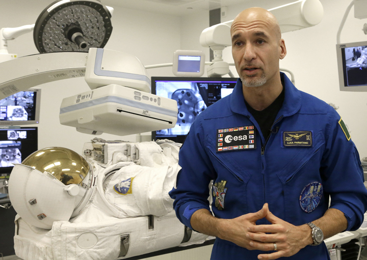 Italian astronaut Luca Parmitano stands beside his space suit sitting under a medical imaging scanner Monday, Dec. 8, 2014, in Houston as he talks about his 2013 space walk when he nearly drowned in his helmet.